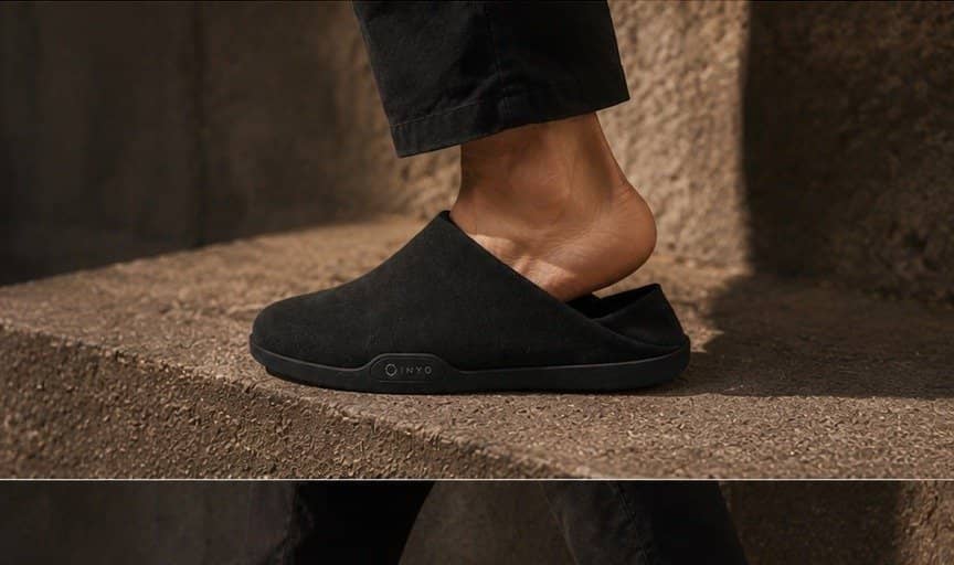 A heel pressing the collapsible panel of a black mule.